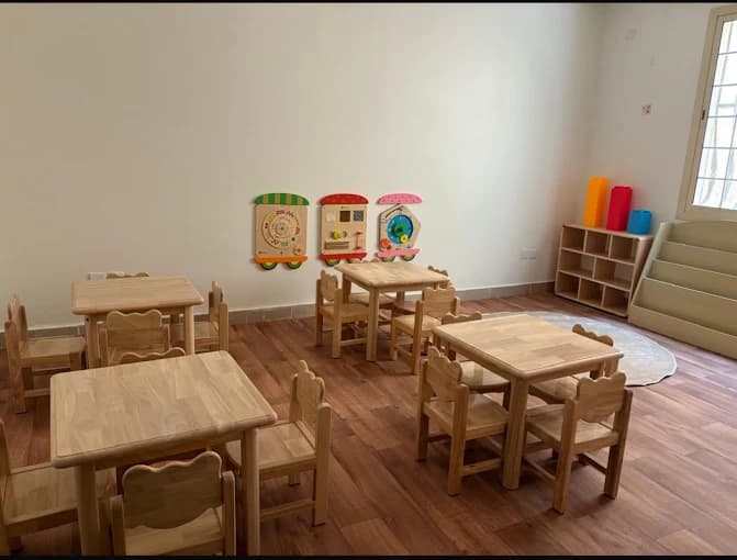 صف دراسي مضيء بطاولات وكراسي خشبية للأطفال وجدران تفاعلية وتخزين منظم
