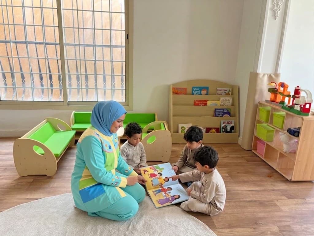 مربية تقرأ قصة لمجموعة أطفال في صف مضيء بمكتبة ورفوف ألعاب